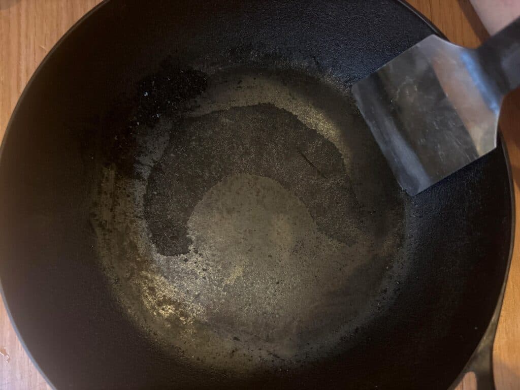 Japanese cast iron pan mid-scrape, carbon layer still in the centre